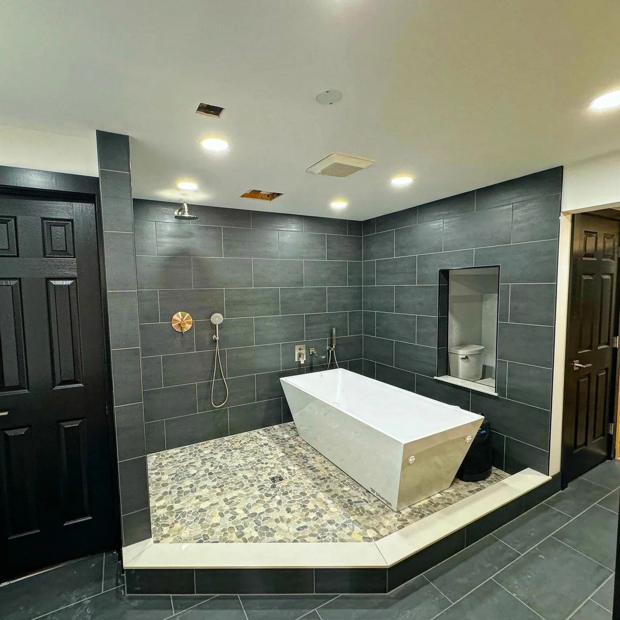 Modern bathroom with dark tile and pebble shower floor.