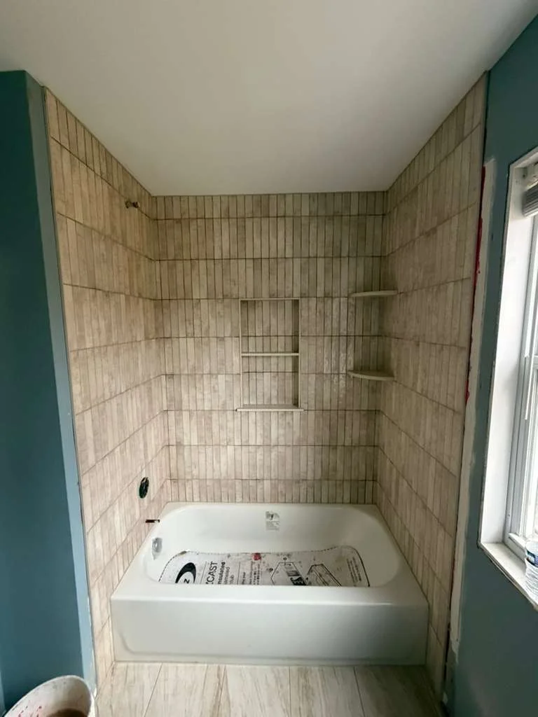 Bathroom with light brown vertical subway tile shower, built-in niche, and white bathtub. by Vicentino Ceramic Tile in Bryn M