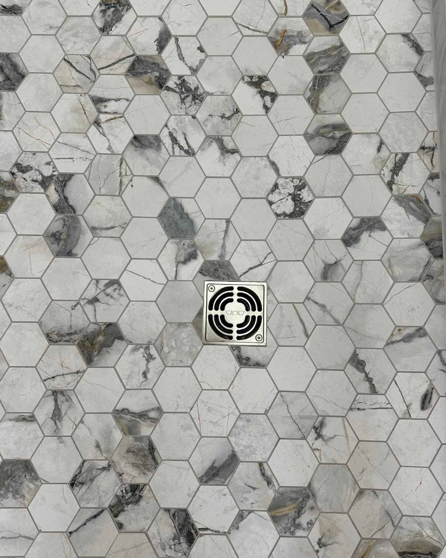 Hexagon marble tile shower floor with a chrome square drain in the center. by Vicentino Ceramic Tile in Bryn Mawr, PA