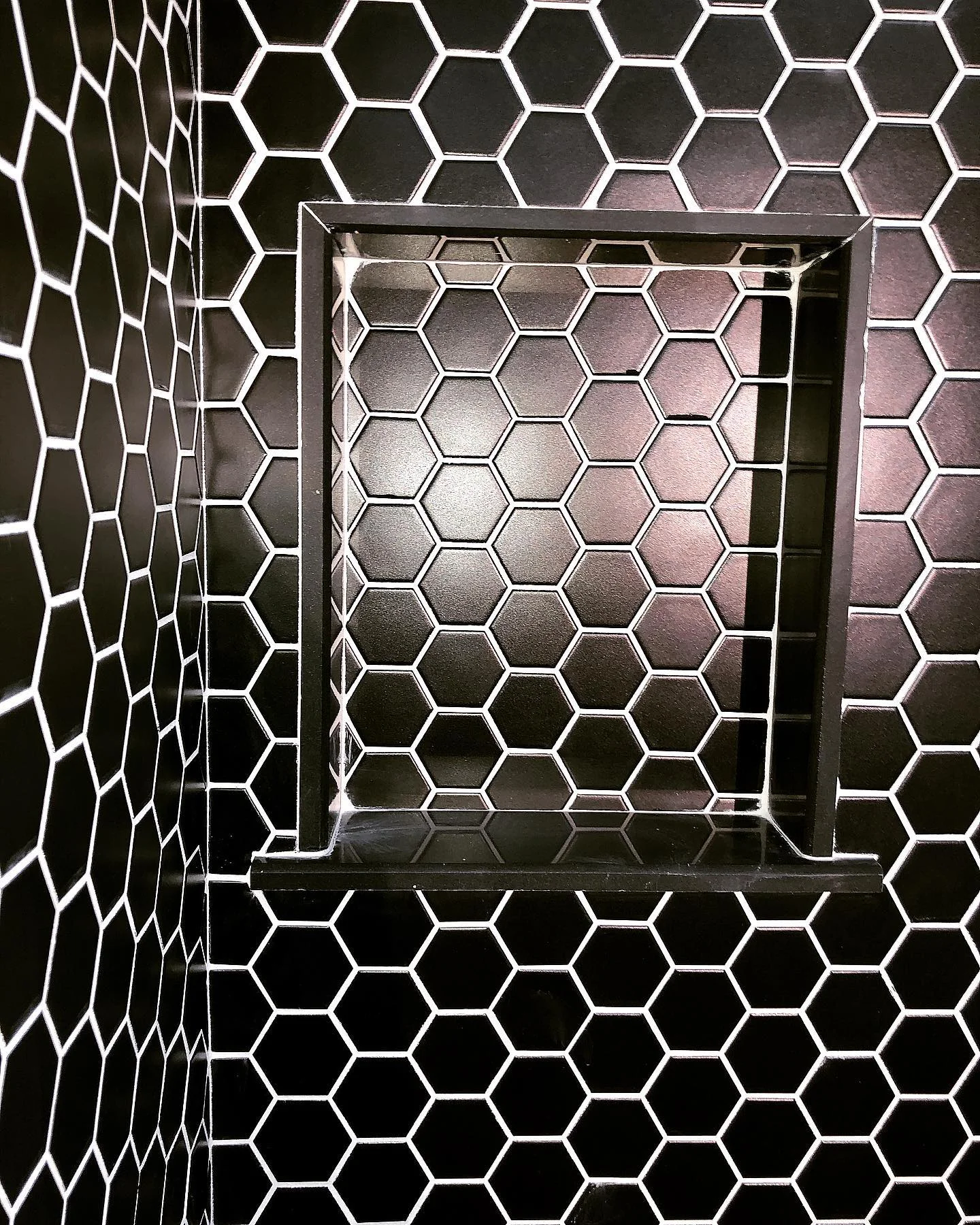 Modern shower niche with black hexagonal tiles and white grout in a bathroom. by Vicentino Ceramic Tile in Newtown, PA