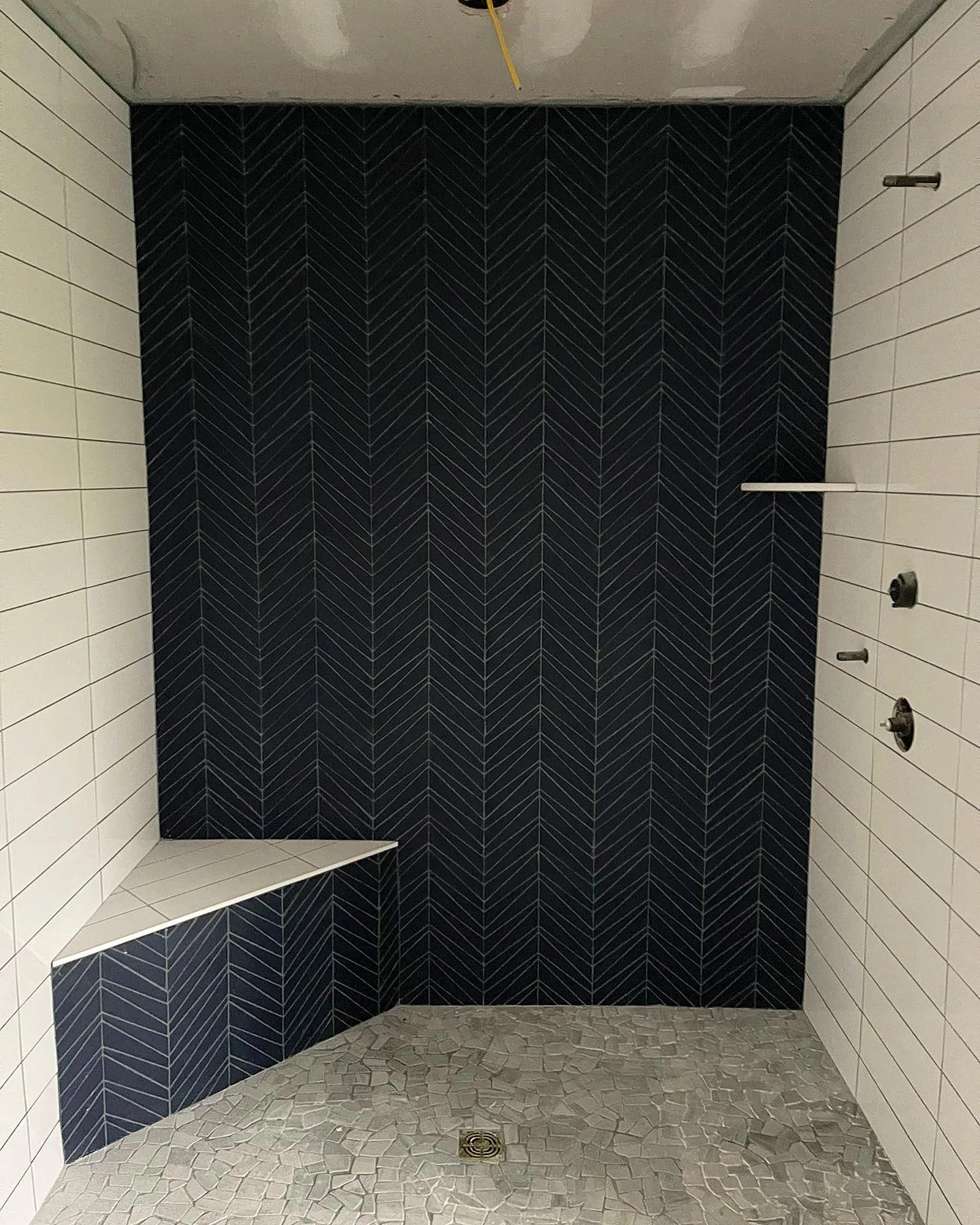 Modern shower with dark blue herringbone tile accent wall and light gray floor. by Vicentino Ceramic Tile in Huntingdon