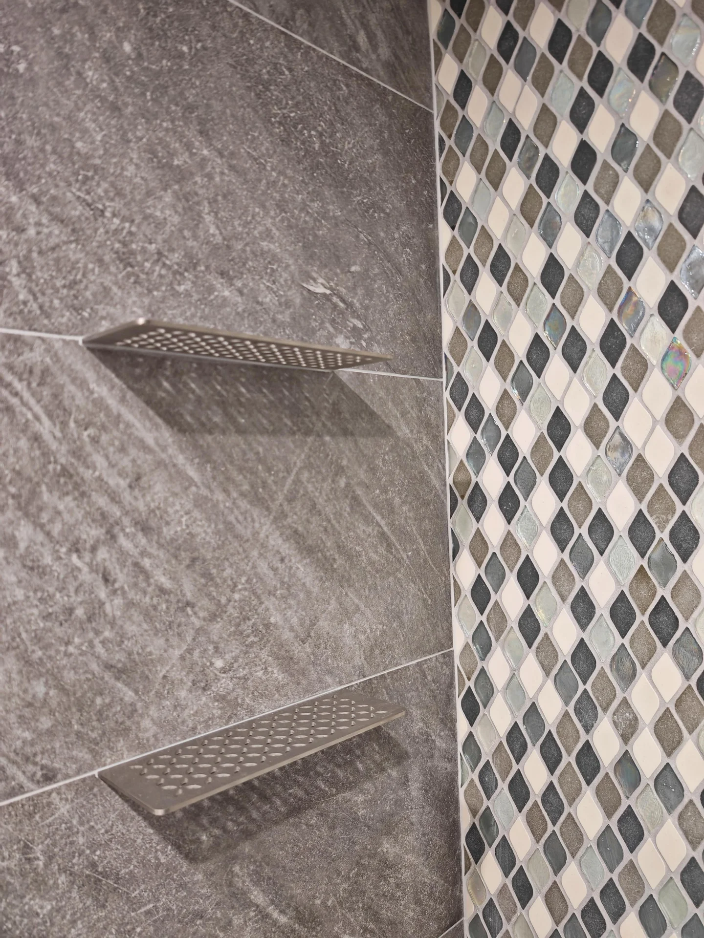 Modern shower with large format grey tile, mosaic accent, and two metal shelves. by Vicentino Ceramic Tile in Ambler, PA