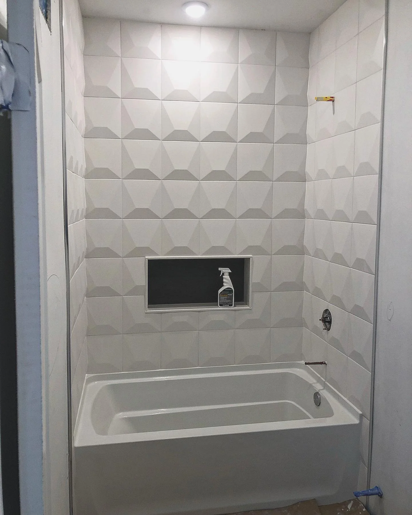 Modern white geometric tile shower surround with built-in niche and new bathtub installation. by Vicentino Ceramic Tile