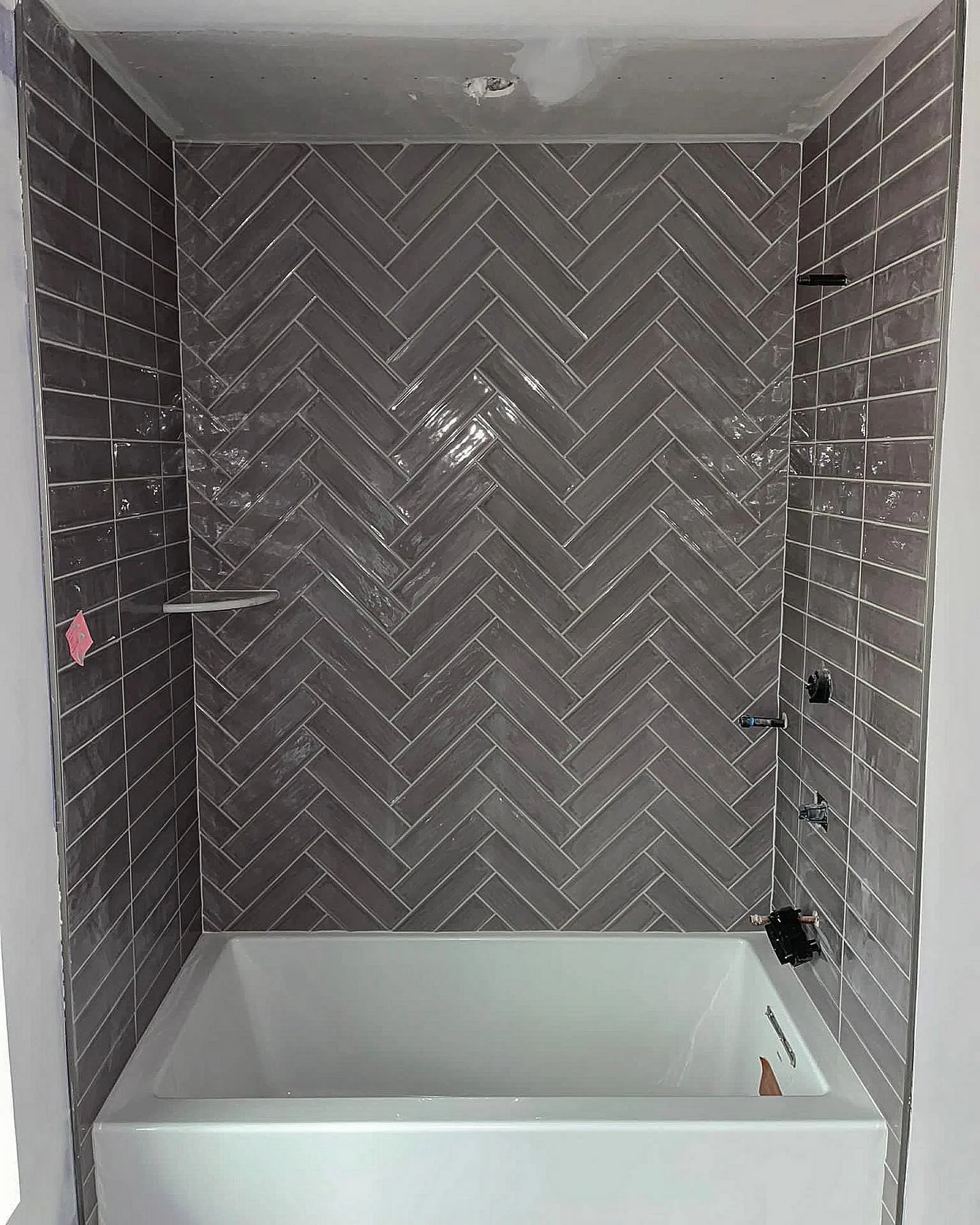 Newly tiled shower with gray subway tiles in a herringbone pattern above a white tub. by Vicentino Ceramic Tile in Wayne