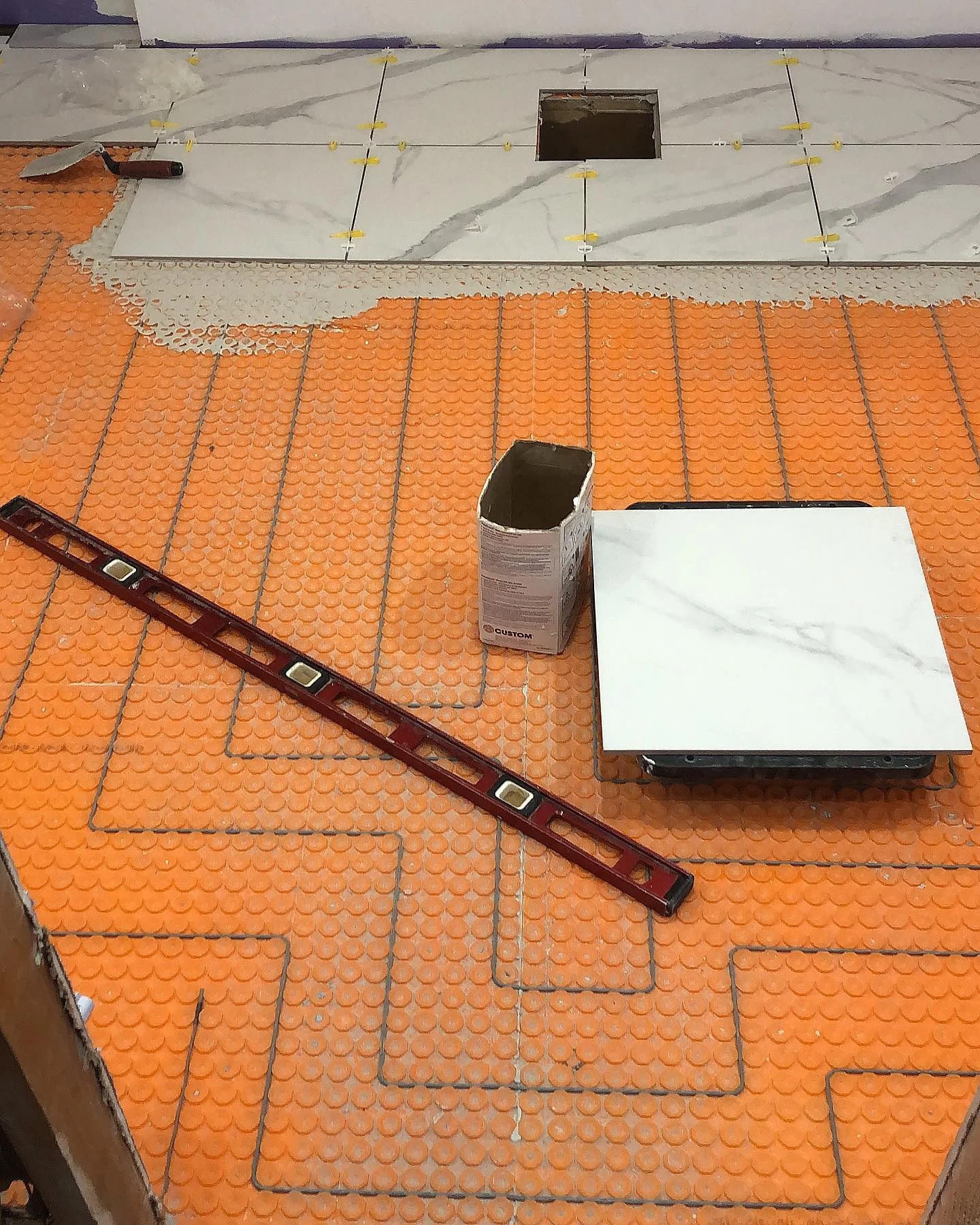 White marble-look tiles installed over orange schluter ditra-heat matting with thin-set. by Vicentino Ceramic Tile in Ya