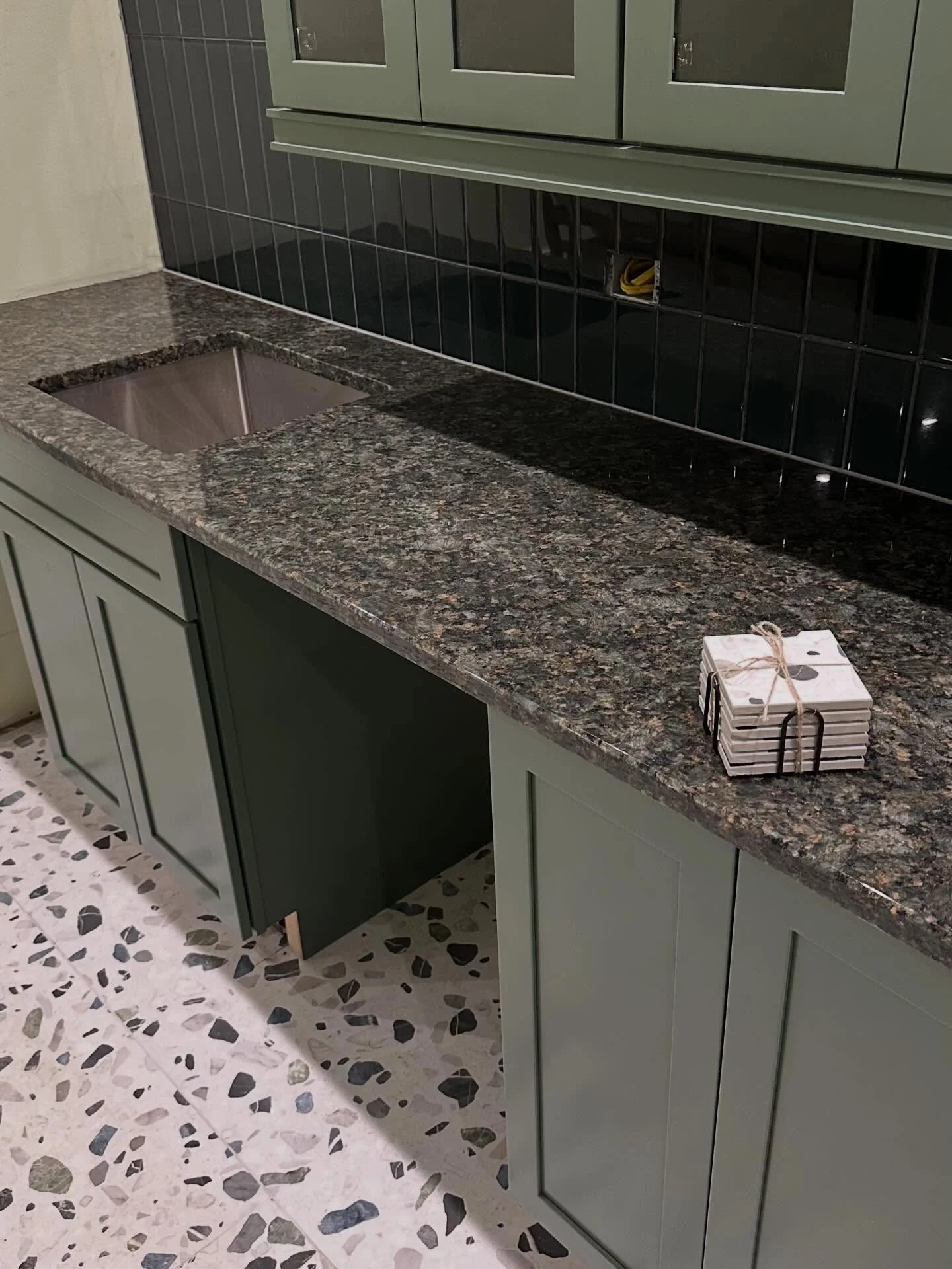 Dark green subway tile backsplash with granite countertop and sage green cabinets in a kitchen. by Vicentino Ceramic Tile in