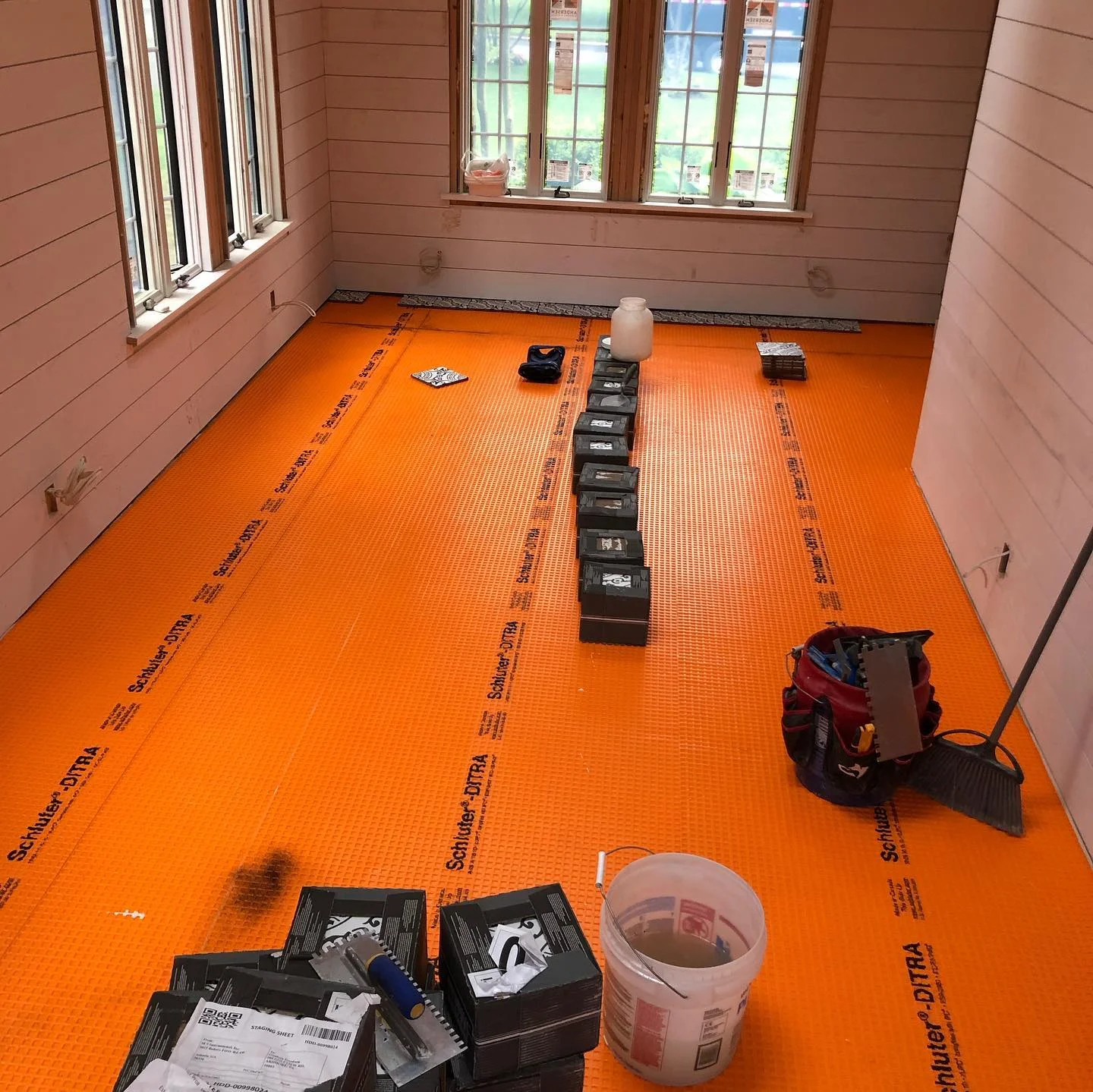 Orange schluter ditra membrane installed on a floor in a room with white paneled walls. by Vicentino Ceramic Tile in Wayne, P