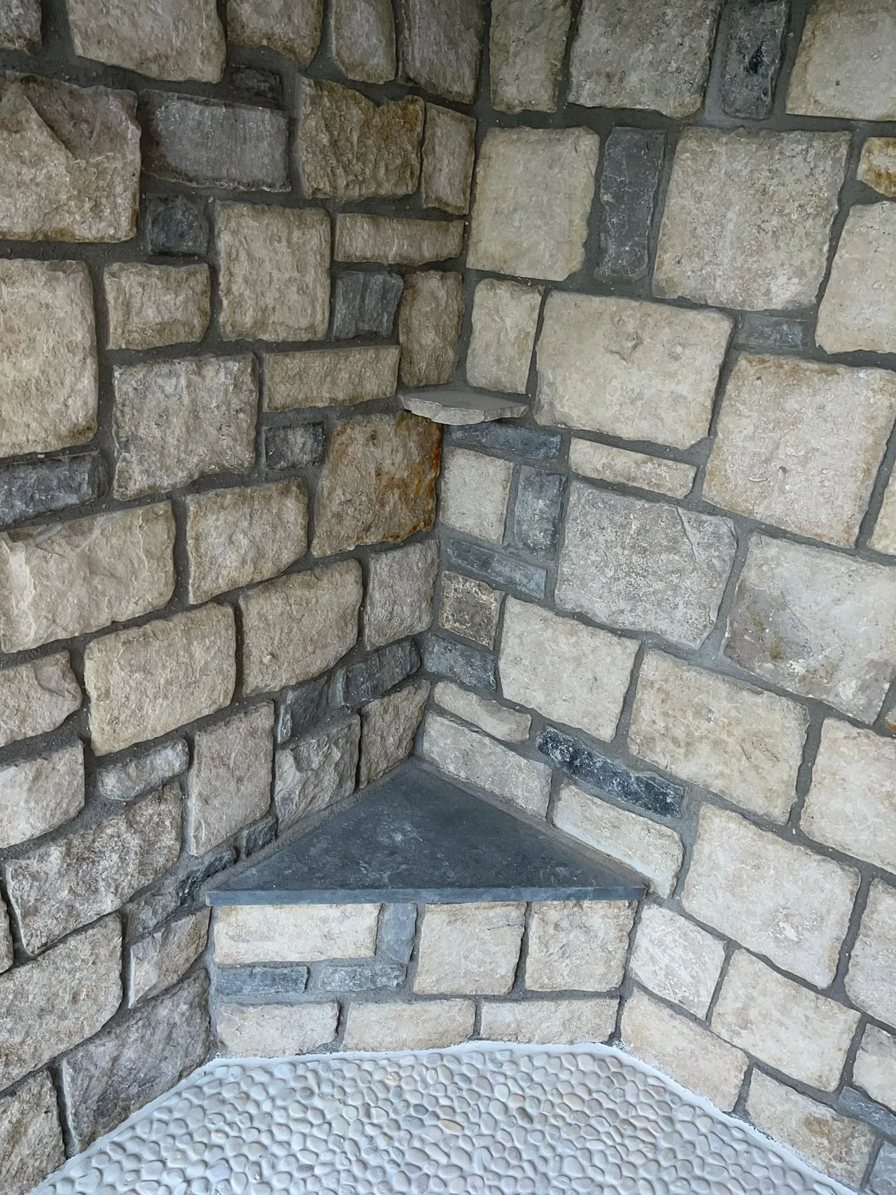 Stone shower wall with corner shelf and pebble floor.