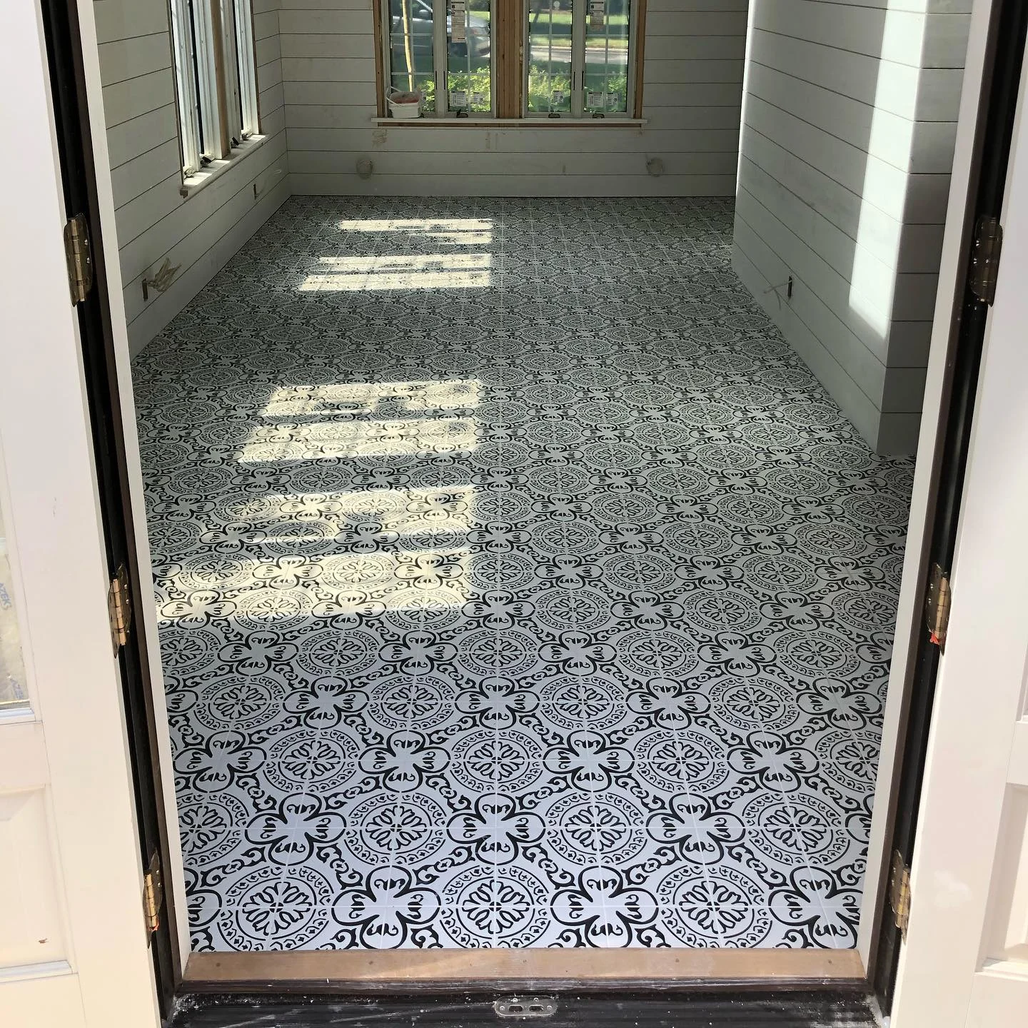 Black and white patterned tile flooring in a sunlit room with white shiplap walls. by Vicentino Ceramic Tile in Ambler, PA