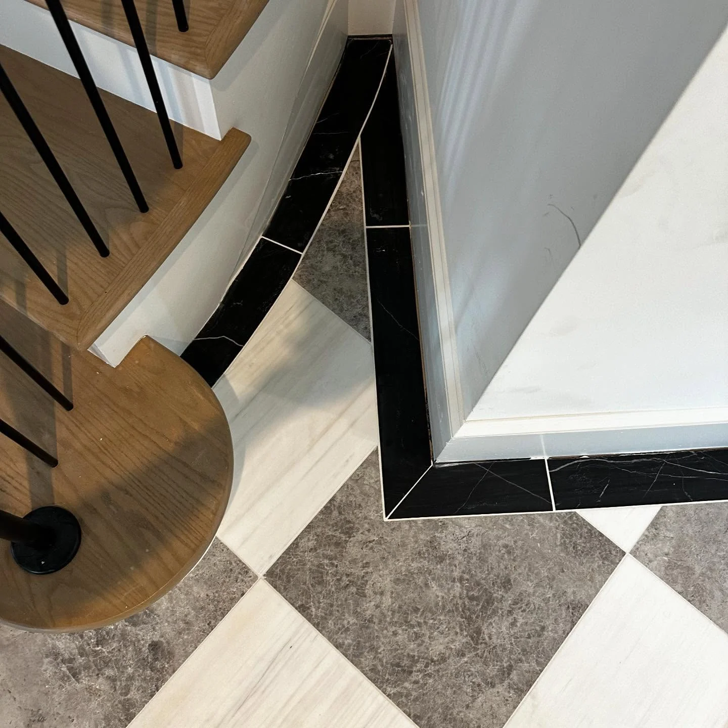 High-contrast black, white, and gray marble tile flooring with custom pattern and wood stairs. by Vicentino Ceramic Tile