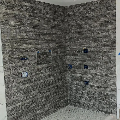 Grey rectangular mosaic tile shower walls with a built-in niche and small floor tiles. by Vicentino Ceramic Tile in Newtown,