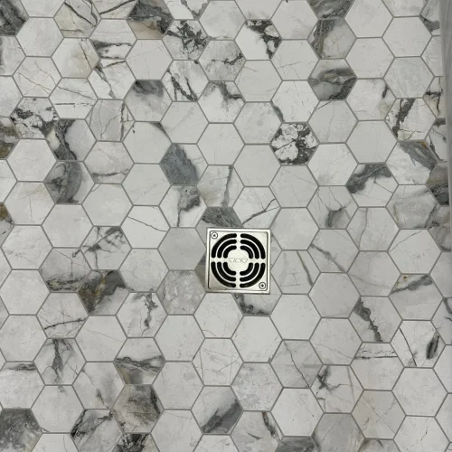 Hexagon marble tile shower floor with a chrome square drain in the center. by Vicentino Ceramic Tile in Bryn Mawr, PA
