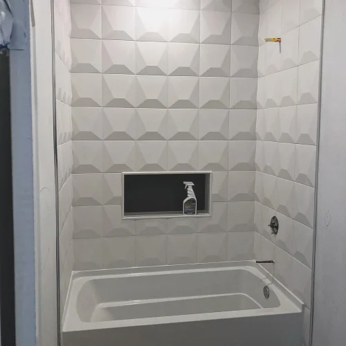 Modern white geometric tile shower surround with built-in niche and new bathtub installation. by Vicentino Ceramic Tile in Br