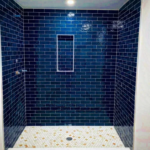 Newly tiled shower with dark blue subway tiles and white hexagonal floor tiles. by Vicentino Ceramic Tile in Haddonfield, NJ