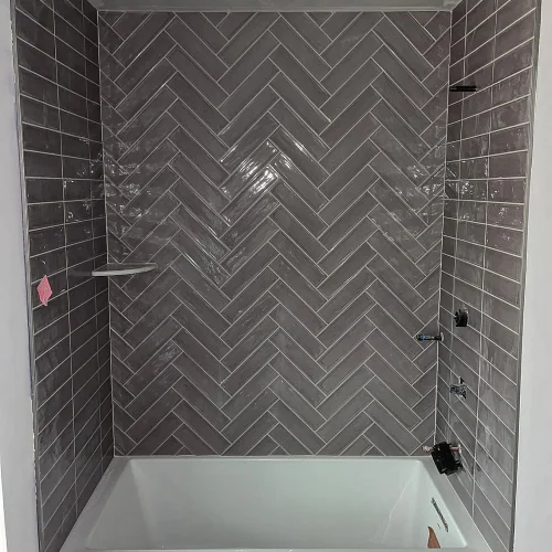 Newly tiled shower with gray subway tiles in a herringbone pattern above a white tub. by Vicentino Ceramic Tile in Wayne, PA