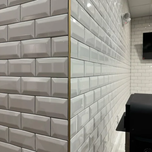 Crisp white subway tile walls with a decorative gold trim corner accent. by Vicentino Ceramic Tile in Haddonfield, NJ